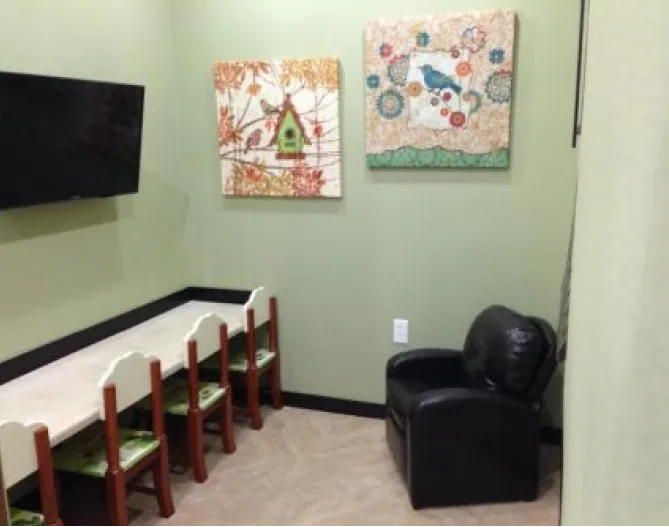 The children's waiting area at the practice: a row of small wooden chairs along a low bench, a television on the wall, and two bird paintings.